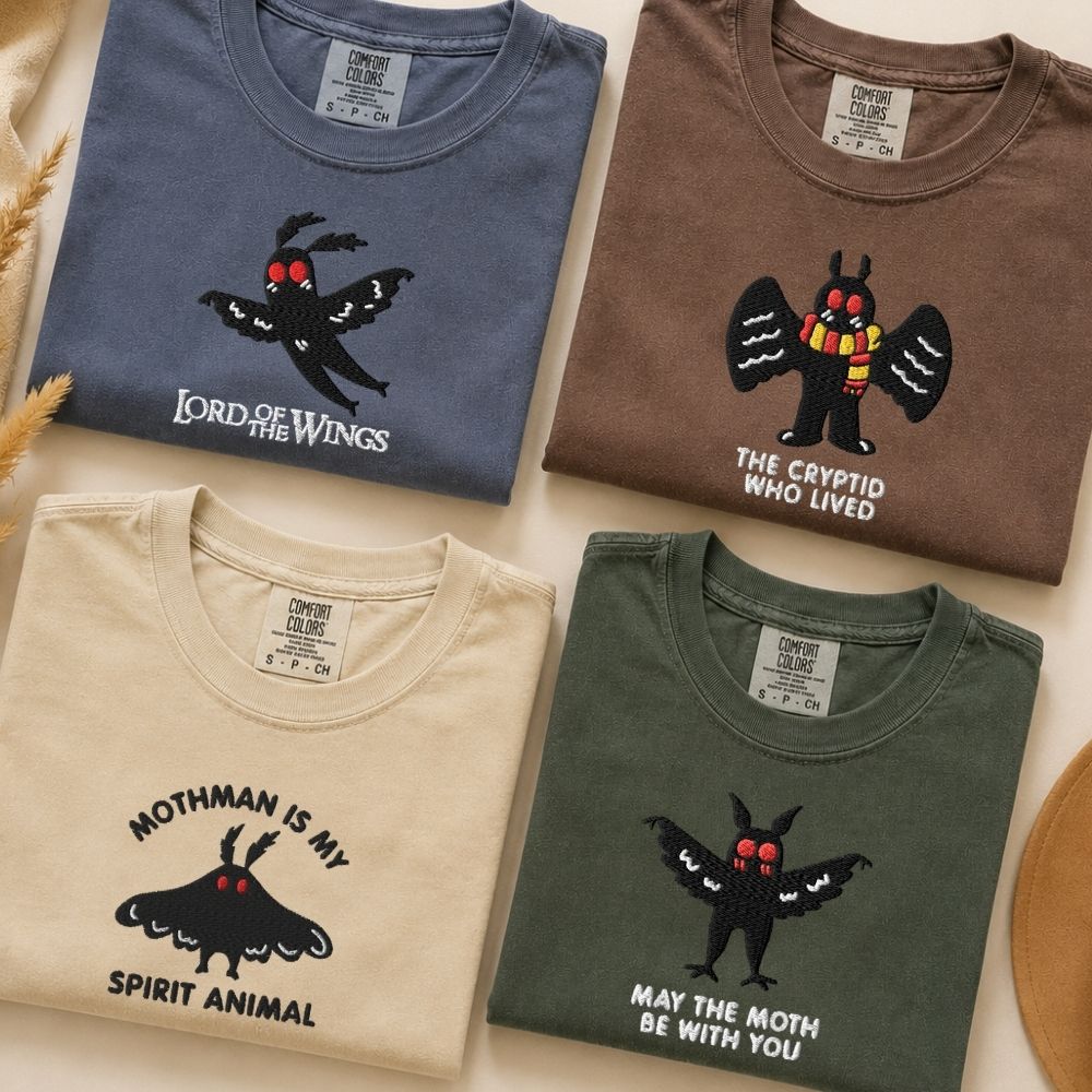 Four folded graphic T-shirts in muted blue, brown, cream, and green, featuring moth-themed embroidered designs. The shirts have playful phrases like “Lord of the Wings,” “Mothman is My Spirit Animal,” and “May the Moth Be With You.”