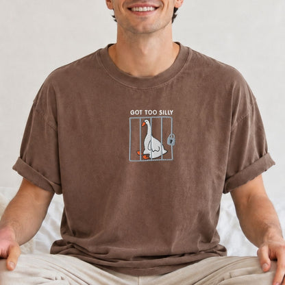 A man wearing a brown crewneck t-shirt with a graphic of a goose in a cage and the text 'GOT TOO SILLY'.