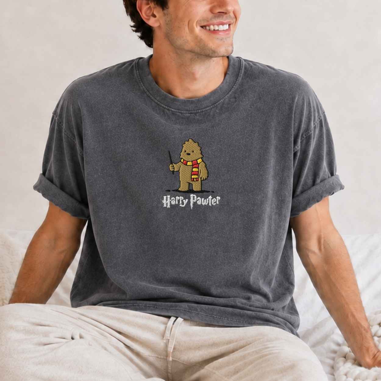 A man wearing a gray t-shirt with a cartoon graphic of a bigfoot  wearing a red and yellow striped scarf and the text 'Harry Pawter' underneath.