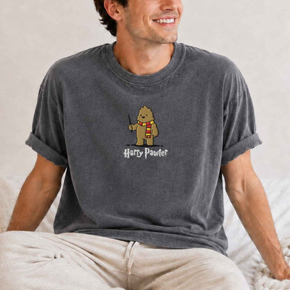 A man wearing a gray t-shirt with a cartoon graphic of a bigfoot  wearing a red and yellow striped scarf and the text 'Harry Pawter' underneath.