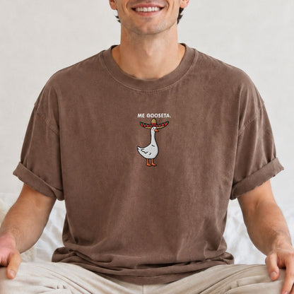 A man wearing a brown crewneck t-shirt with a graphic of a white goose wearing a sombrero and the text 'Me Gooseta'.