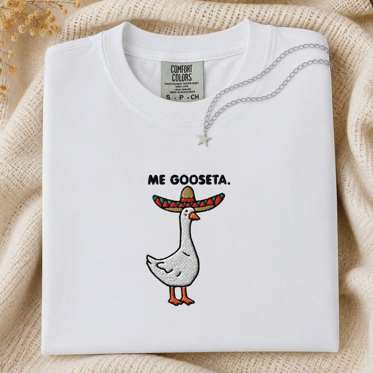 A folded white Comfort Colors t-shirt with a graphic of a goose wearing a sombrero and the text 'ME GOOSETA.' printed on the chest.