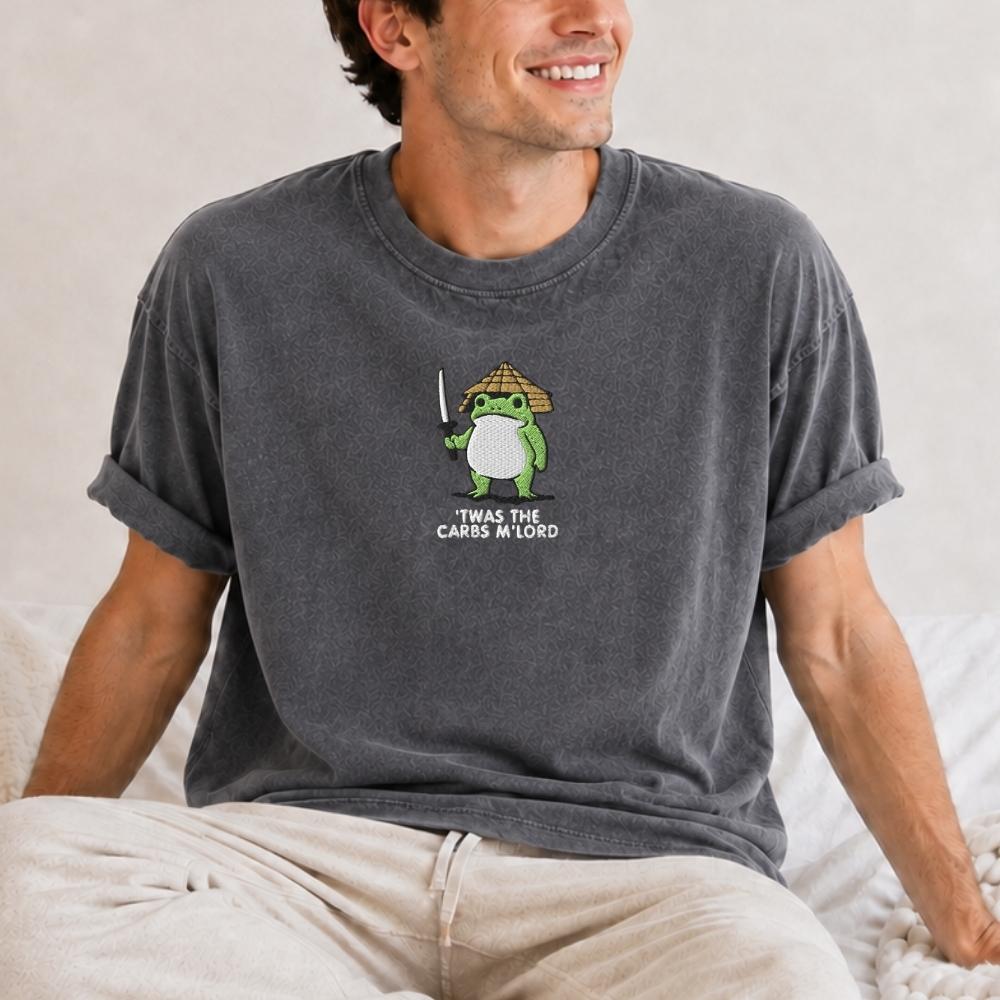 A man wearing a dark gray washed graphic t-shirt with a cartoon frog holding a sword and the text 'IT WAS THE CARS MY LORD'.