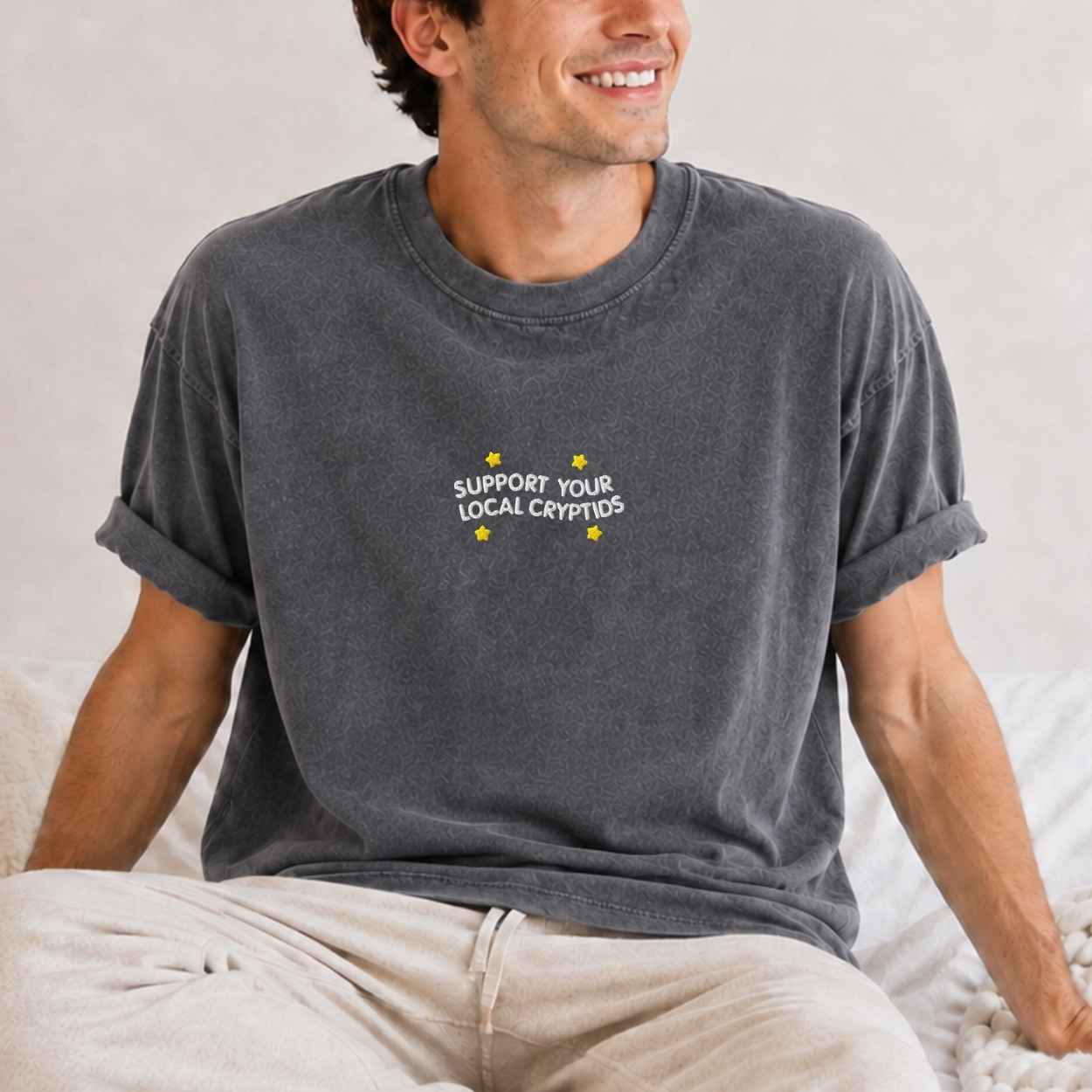 A man wearing a dark gray graphic t-shirt with a text 'support your local cryptids'.